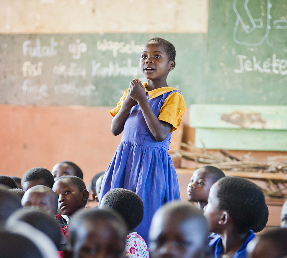 A photo of a young girl speaking up in her classroom